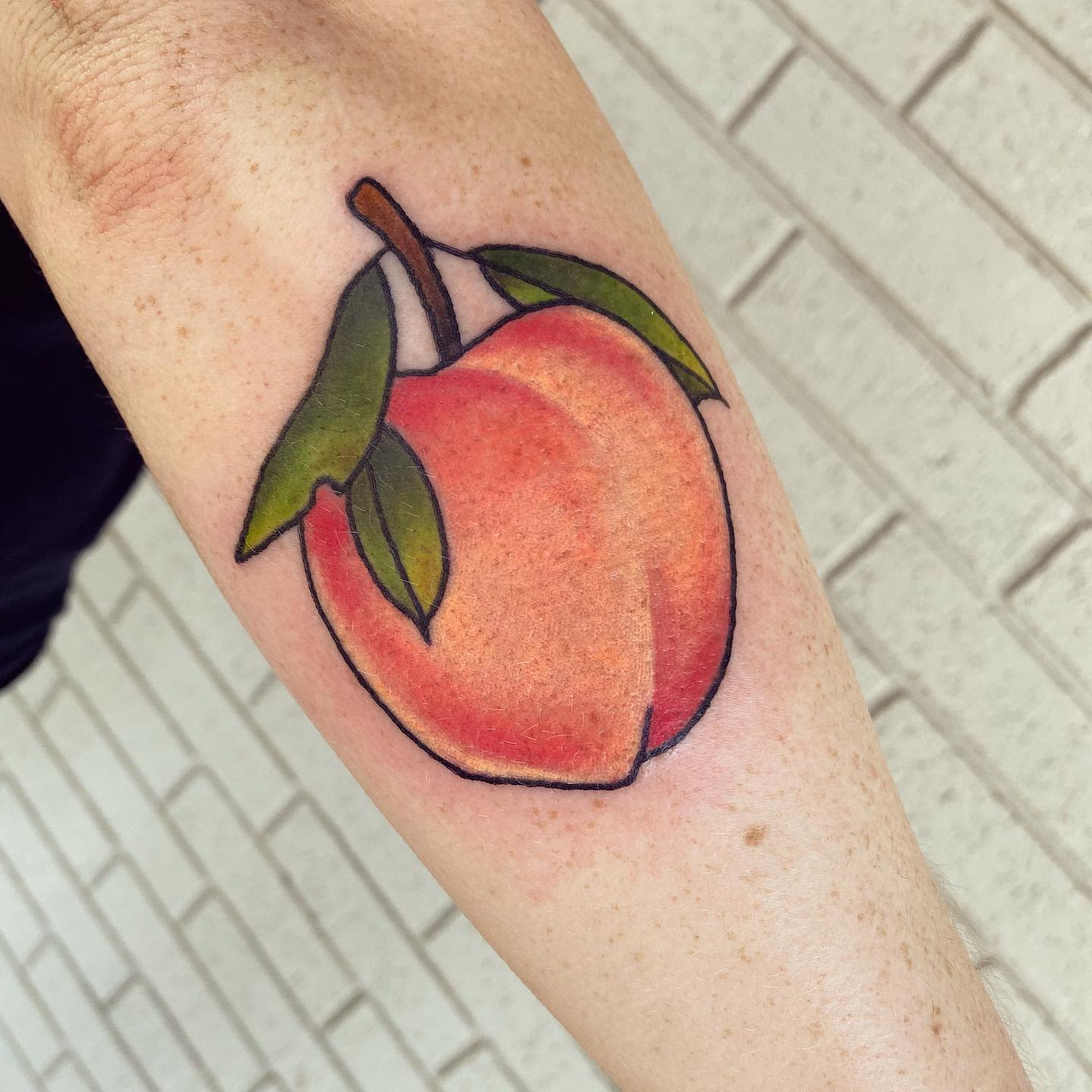 A colorful tattoo of a peach with leaves on a forearm